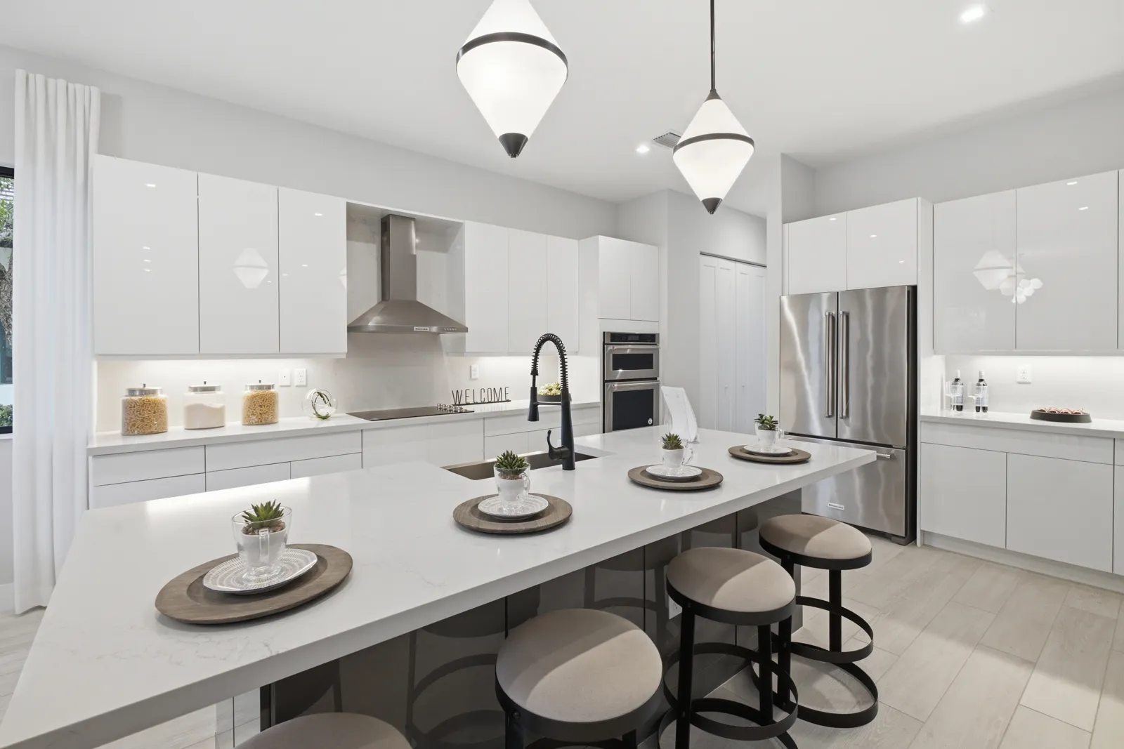 White kitchen with a long island, black faucet and pendant lights